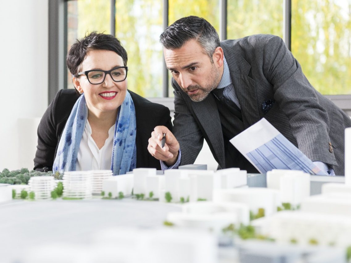 Man and woman talking about a new building project pointing at an architectural model