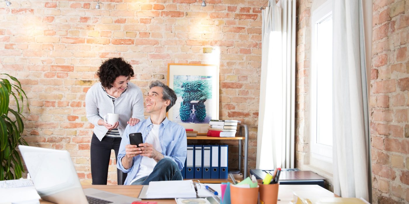 Man with phone in conversatuion with woman in front of brick-lined wall