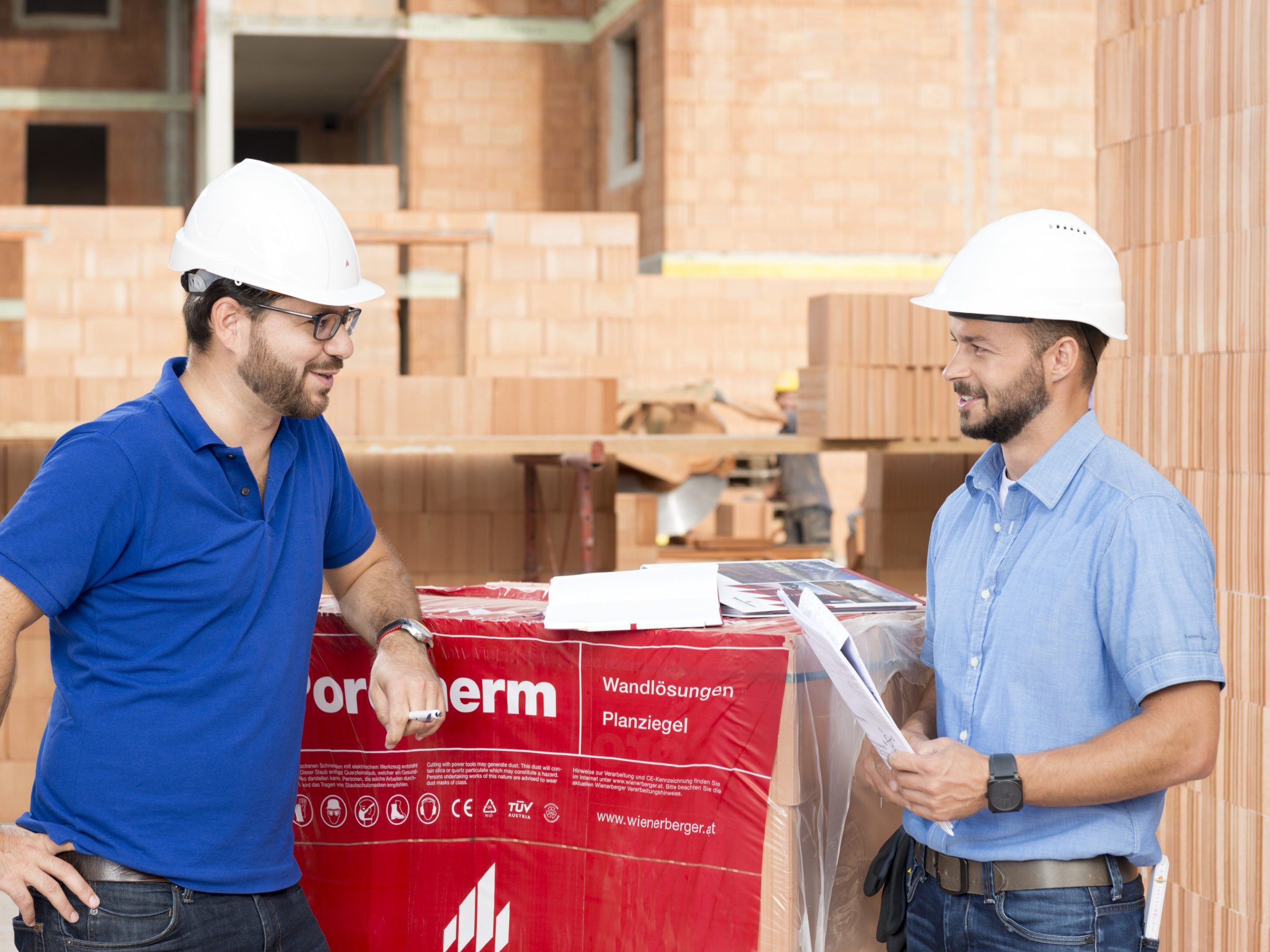 Building professionals talking at construction site next to foil wrapped pallette of brick blocks. > There is another version of this image available with another worker in the background
