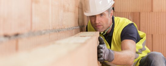 Construction worker checking alignment of mineral-wool filled clay block